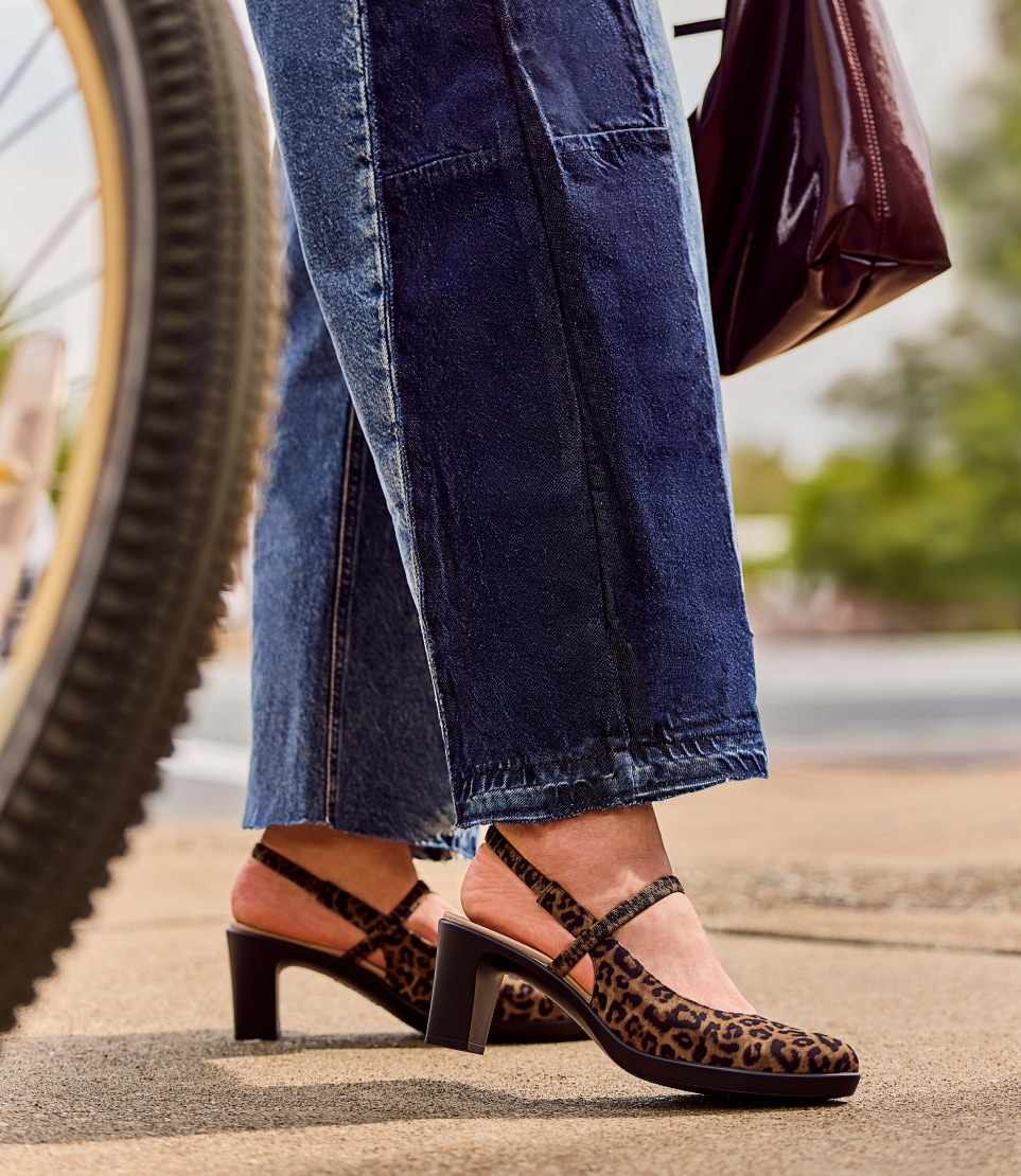 a model wearing leopard print LifeStride heels while carrying a purse next to a bicycle wheel